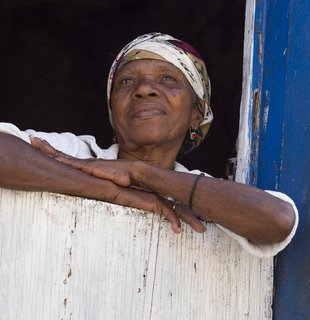 Eine ältere einheimische Frau lehnt sich aus einem Fensterrahmen und schaut hinaus
