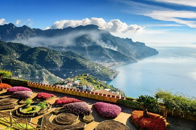 Von einem Garten mit bunten Blumenbeeten aus schaut man einen Abhang hinunter auf das Meer vor Ravello.