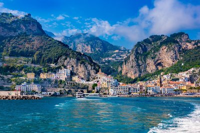 Über das leuchtendblaue Meer im Vordergrund schaut man auf das Stadtpanorama von Amalfi.