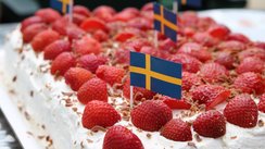 Eine eckige Sahnetorte ist mit Erdbeeren belegt und Schwedenflaggen geschmückt.