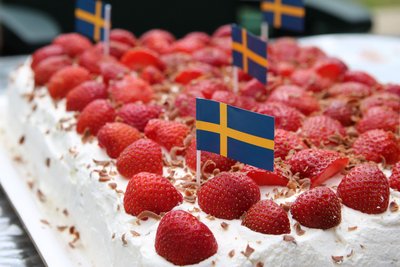Eine eckige Sahnetorte ist mit Erdbeeren belegt und Schwedenflaggen geschmückt.