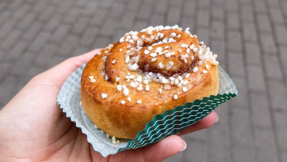 Eine schwedische Zimtschnecke (Kanelbullar) Eine Hand hält eine schwedische Zimtschnecke in die Kamera