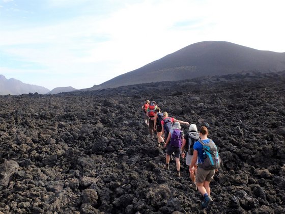 Wandern durch Fogos Vulkanlandschaft Durch schwarzes Lavageröll läuft eine Wandergruppe hügelan.
