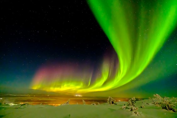 Am unteren Bildrand zieht sich eine Schneelandschaft hin; die oberen vier Fünftel des Bildes nimmt der Himmel ein, über dem sich ein sich von links unten nach rechts oben verbreiterndes grünes Nordlicht erstreckt.