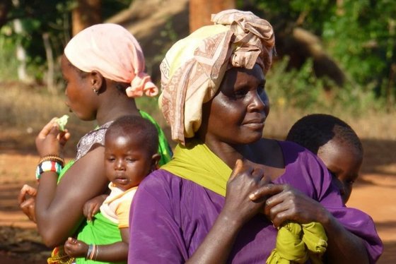 Dorfbewohnerin in Tansania Zwei afrikanische Frauen mit Kopftüchern stehen Rücken an Rücken gegeneinander und haben jeweils ein Kleinkind in einem Tragetuch auf dem Rücken.