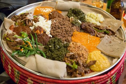 Injera gibt es vegetarisch mit Linsen, Erbsen- und Geüsecurrys Angerichtet auf einem Fladenbrot sieht man verschiedene Gemüse, Pasten und Saucen.