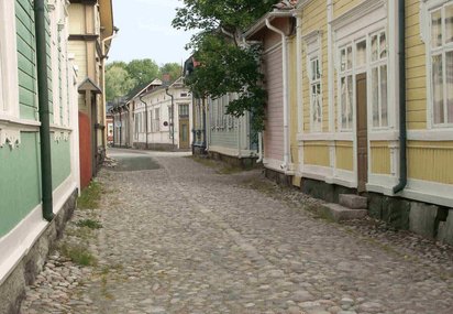 An einer mit Kopfstein gepflasterten Straße liegen links und rechts bunte Holzhäuser hintereinander.