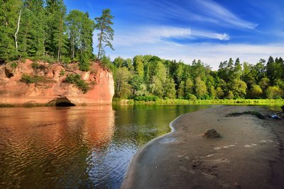 Sandiges Flussufer mit Sandstein und Wald im Hintergrund