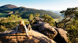 Eine Frau sitzt auf einem Felsen und genießt den Ausblick auf den Pfälzerwald