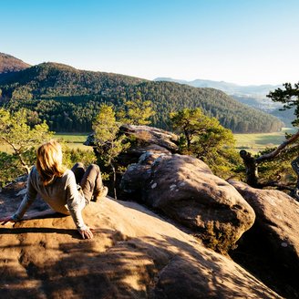 Eine Frau sitzt auf einem Felsen und genießt den Ausblick auf den Pfälzerwald