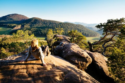 Eine Frau sitzt auf einem Felsen und genießt den Ausblick auf den Pfälzerwald