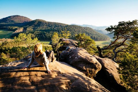 Eine Frau sitzt auf einem Felsen und genießt den Ausblick auf den Pfälzerwald