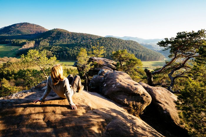 Eine Frau sitzt auf einem Felsen und genießt den Ausblick auf den Pfälzerwald