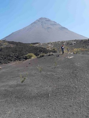 Hiuter einem Gesteinsfeld mit Lavageröll erhebt sich ein karger Vulkankegel in den blauen Himmel.