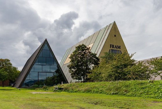 Auf einer Wiese stehen zwei dreieckige Gebäude, das linke hat eine komplett verglaste Fassade.
