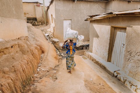 Frau trägt einen Sack auf dem Kopf durch eine kleine Gasse in Kigali.