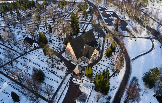 Luftaufnahme einer Kirche in gedrungener Kreuzform auf einem verschneiten Friedhof.