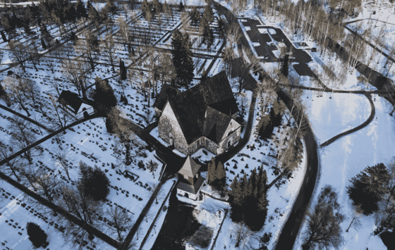 Luftaufnahme einer Kirche in gedrungener Kreuzform auf einem verschneiten Friedhof.