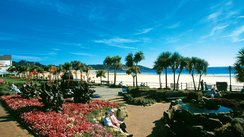 Menschen sitzen auf einem mit Blumen schön angelegten Platz auf einer Strandpromenade auf Jersey