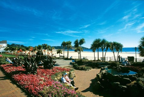 Menschen sitzen auf einem mit Blumen schön angelegten Platz auf einer Strandpromenade auf Jersey