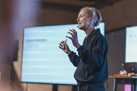 Seitliches Bild einer Frau mit kurzen, blonden Haaren, die eine Präsentation hält.