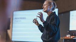 Seitliches Bild einer Frau mit kurzen, blonden Haaren, die eine Präsentation hält.
