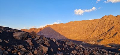 Sonnenaufgang auf dem Pico do Fogo Blick in eine felsige, vom Licht des Sonnenaufgangs ausgeleuchtete Caldera, auf deren Kraterrand die Vulkanspitze einen Schatten wirft