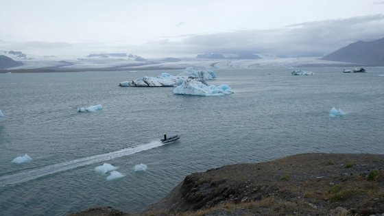 Weite Gletscherlagune Jökulsárlón Ein kleines Motorboot gleitet durch die eisige Gletscherlagune Jökulsárlón unter wolkenverhangenem Himmel.