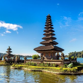 Der Ulun Danu Bratan Tempel steht auf einer kleinen Insel im Bratan-See auf Bali. Der mehrstufige Turm spiegelt sich im ruhigen Wasser. Umgeben vonVegetation und Bergen erstreckt sich der See unter einem klaren Himmel.