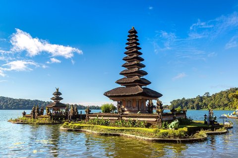 Der Ulun Danu Bratan Tempel steht auf einer kleinen Insel im Bratan-See auf Bali. Der mehrstufige Turm spiegelt sich im ruhigen Wasser. Umgeben vonVegetation und Bergen erstreckt sich der See unter einem klaren Himmel.