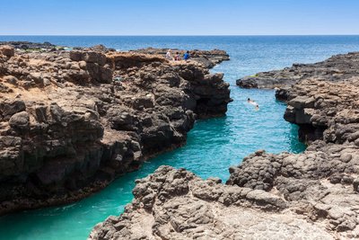 Touristen schwimmen entlang einer steinigen Bucht 
