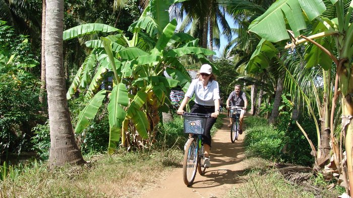 Zwei Touristen fahren mit dem Fahrrad auf einem Weg zwischen Palmen