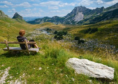 Eine Frau erholt sich auf einer Parkbank im Durmitor Nationalpark mit Blick auf den imposanten Sedlo Pass. 