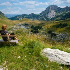 Eine Frau erholt sich auf einer Parkbank im Durmitor Nationalpark mit Blick auf den imposanten Sedlo Pass. 