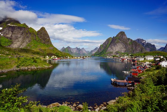 Dorf auf den Lofoten am Fjord in Norwegen links und rechts vom Fjord stehen bunter Häuser, im Hintergrund die Berge