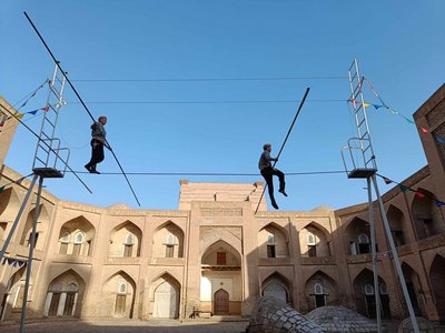 Zwei Seiltänzer zeigen ihre Kunst in einem Innenhof in Chiwa. Über dem Gebäude im Hitnergrund erhebt sich ein leuchtend blauer Himmel.