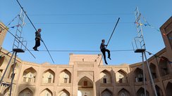 Zwei Seiltänzer zeigen ihre Kunst in einem Innenhof in Chiwa. Über dem Gebäude im Hitnergrund erhebt sich ein leuchtend blauer Himmel.