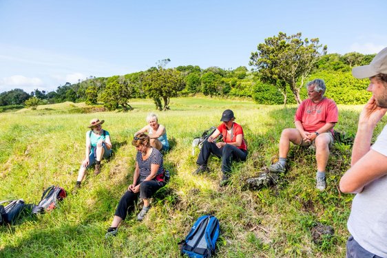 Reisegruppe sitzt auf einer Wiese und erholt sich von einer Wanderung.