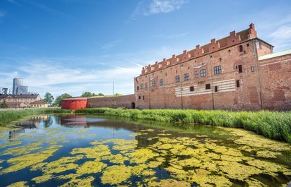 Das Kastell Malmöhus Im Vordergrund befindet sich eine mit Entengrütze bedeckte Wasserfläche, rechts dahinter erstreckt sich in die Bildtiefe hinein ein trutziges Gebäude.