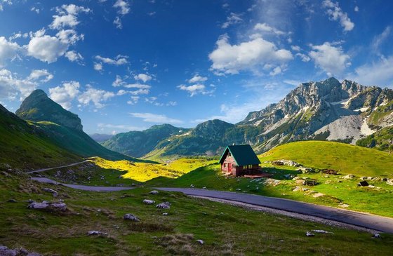 Blick auf ein Tal mit Hütte vor den Durmitor Bergen unter klarem, blauen Himmel in Montenegro.