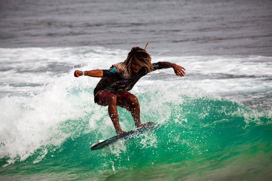 Ein kapverdischer Surfer stürzt sich in die Wellen Ein Surfer reitet auf einer türkisen Welle.