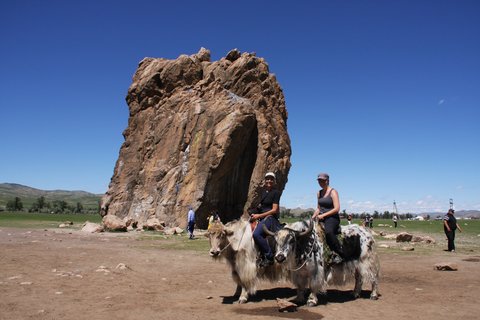 Zwei Touristinnen reiten auf einem Yak an einem Fels vorbei