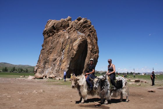 Yak Reiten in der Mongolei Zwei Touristinnen reiten auf einem Yak an einem Fels vorbei