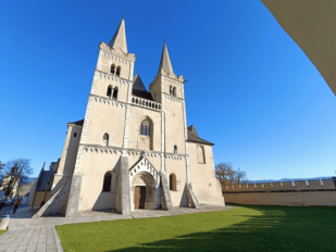 Es erhebt sich eine eher gedrungen wirkende, grau-beige verputzte Kirche, deren Fassade von zwei Türmen geziert wird. Das Bild ist durch einen Filter mit übertriebener Froschperspektive verzerrt, so dass alle Bauelemente zur Bildmitte streben. Der Bildraum vor der Kirche wird durch eine Wiese ausgefüllt, um die Kirche herum blauer Himmel.