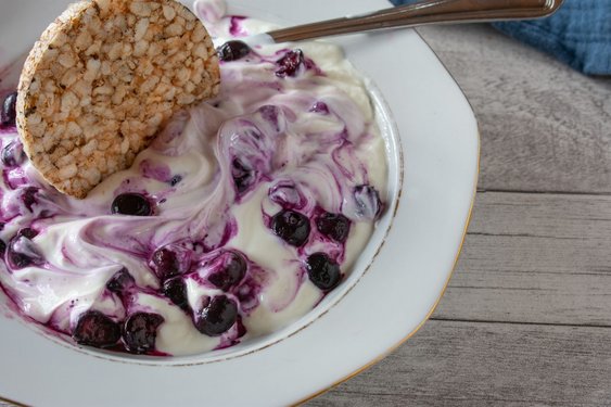 Blaubeeren mit Skyr, worin ein Löffel steckt, auf einem weißen Teller