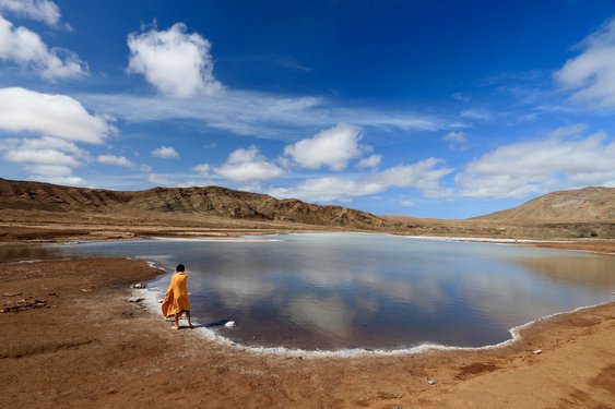 Ein Junge in oranger Kleidung steht vpr der Saline im Krater von Pedra de Lume auf Sal.