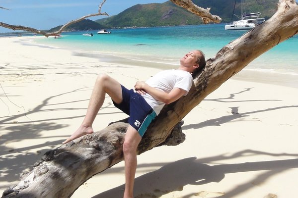 Reiseberater Dennis Markmann angelehnt an einem Baum am Meer.