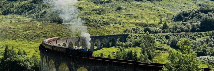 alte Dampflok fährt durch eine Berglandschaft