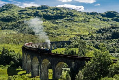 Jakobitenzug auf Aquädukt in den schottischen Highlands in Großbritannien alte Dampflok fährt durch eine Berglandschaft
