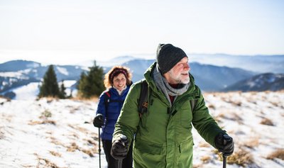 Ein älteres Paar bewegt sich mit Skistöcken ausgerüstet durch eine winterliche Gebirgslandschaft.